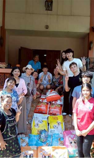 Animal People Alliance volunteers and community members gather on steps behind stacks of donated dog food bags, smiling and making peace signs.